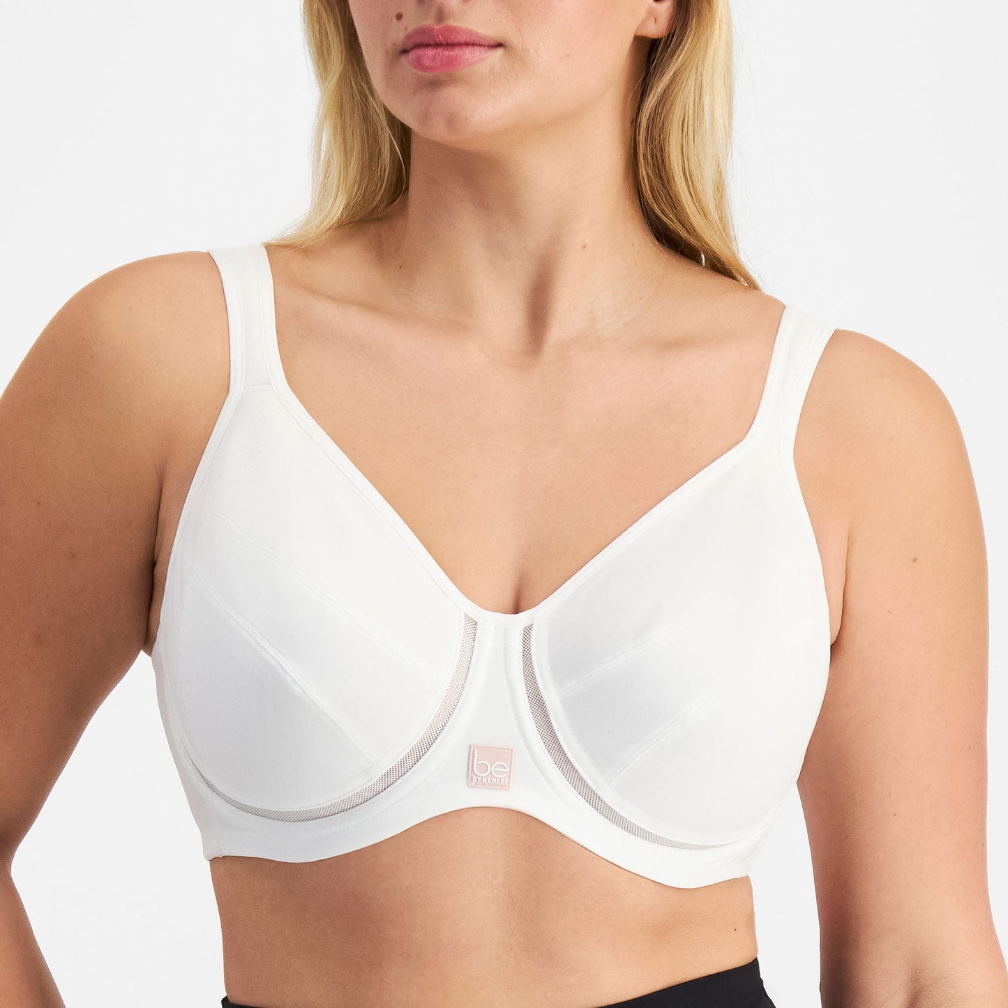 Woman wearing a white Be By Berlei bra and black leggings on a plain background