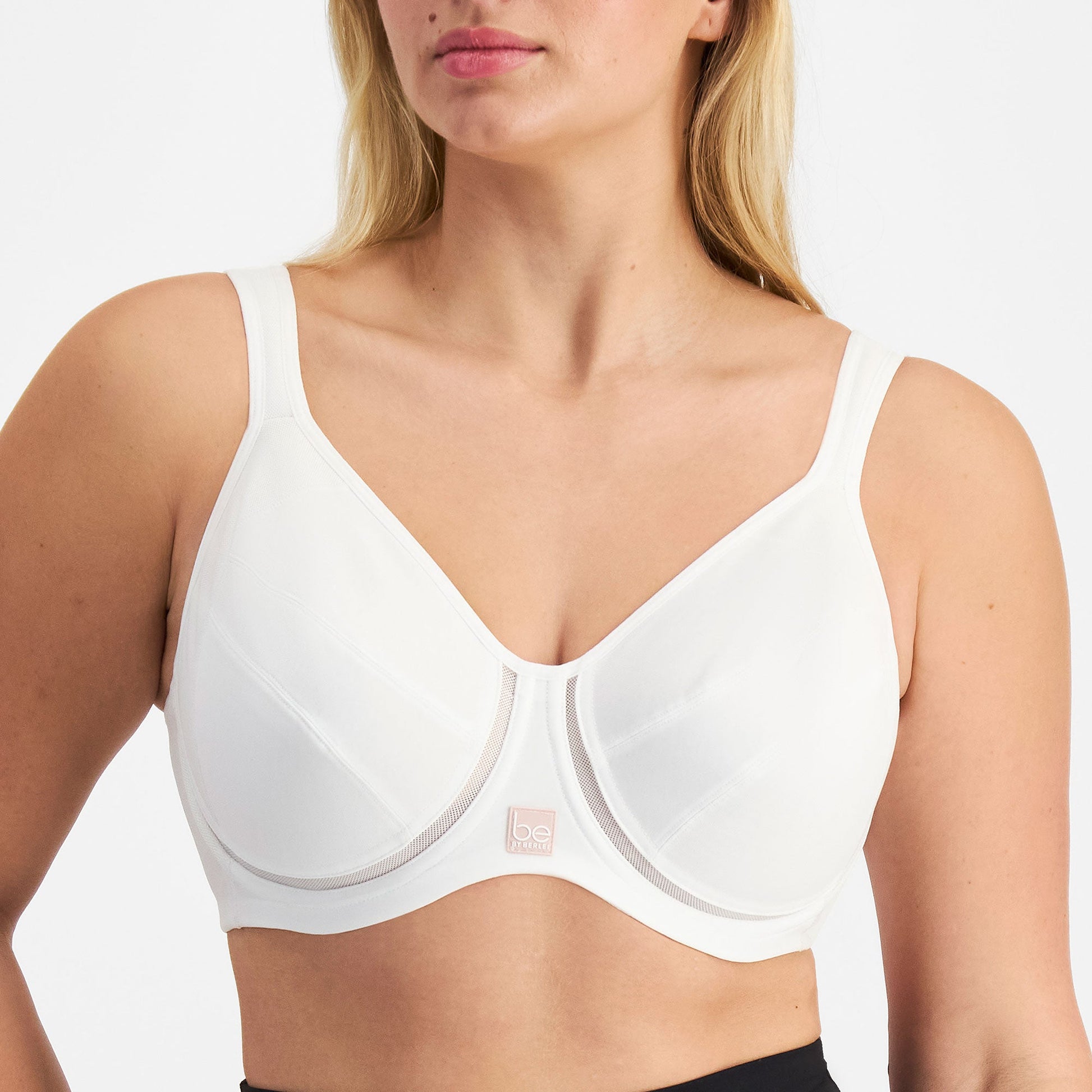 Woman wearing a white Be By Berlei bra and black leggings on a plain background